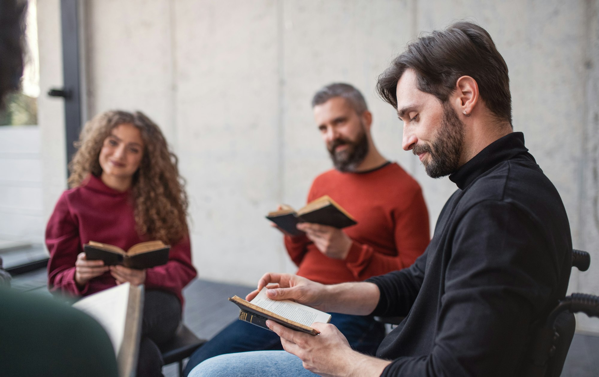 Men and women sitting in circle reading Bible book during group therapy